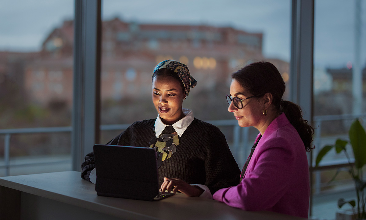 Photo of two women observing the screen of a laptop.