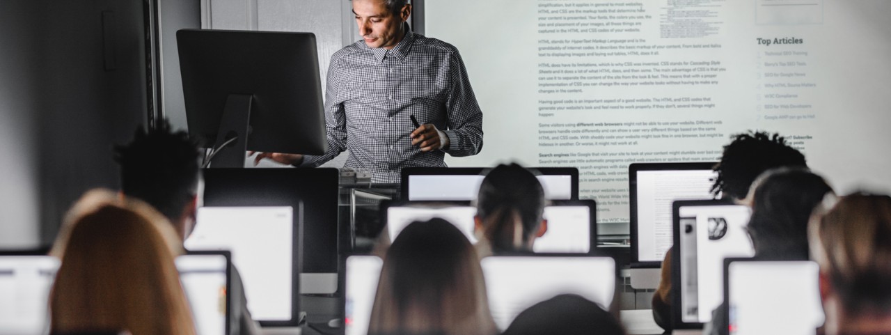 Male teacher giving a lecture from desktop PC during a class at computer lab.