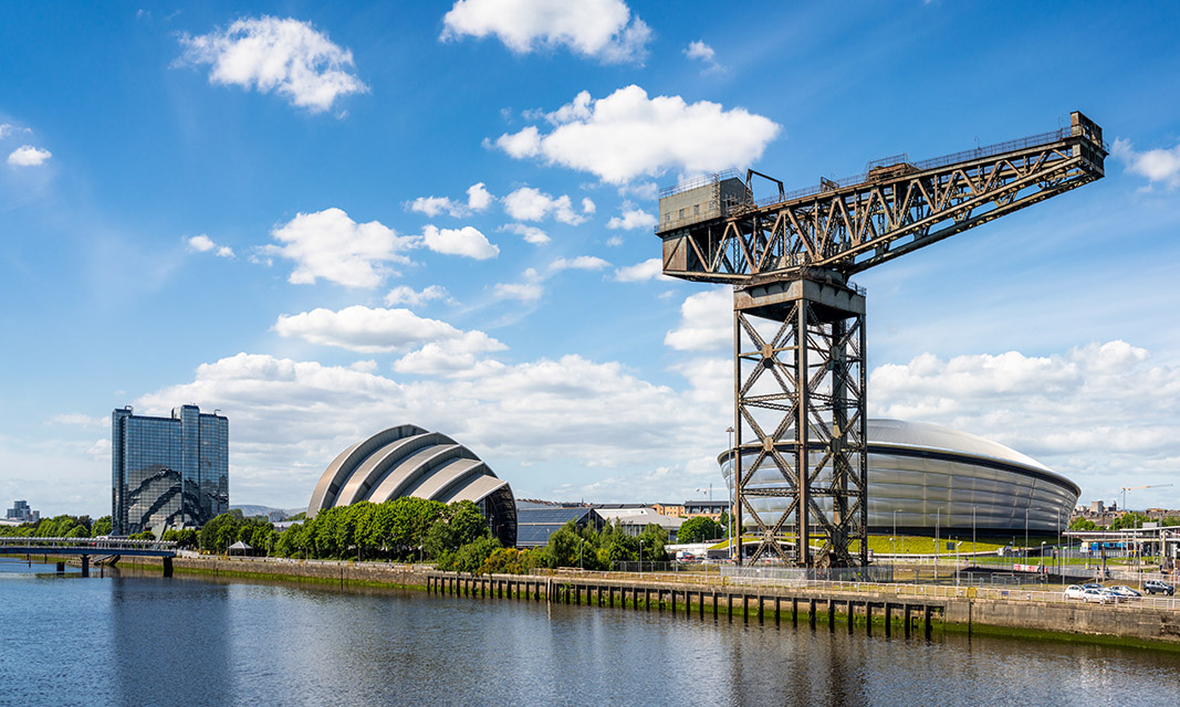 A panoramic view along the north bank of the River Clyde in Glasgow, with hotels, the Hydro, the Armadillo and with the skyline dominated by the historic Finnieston Crane.