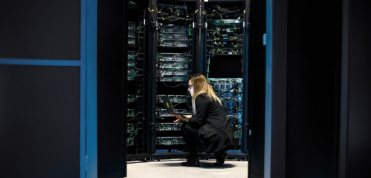 Female IT Professional Working in Server Room With Laptop.