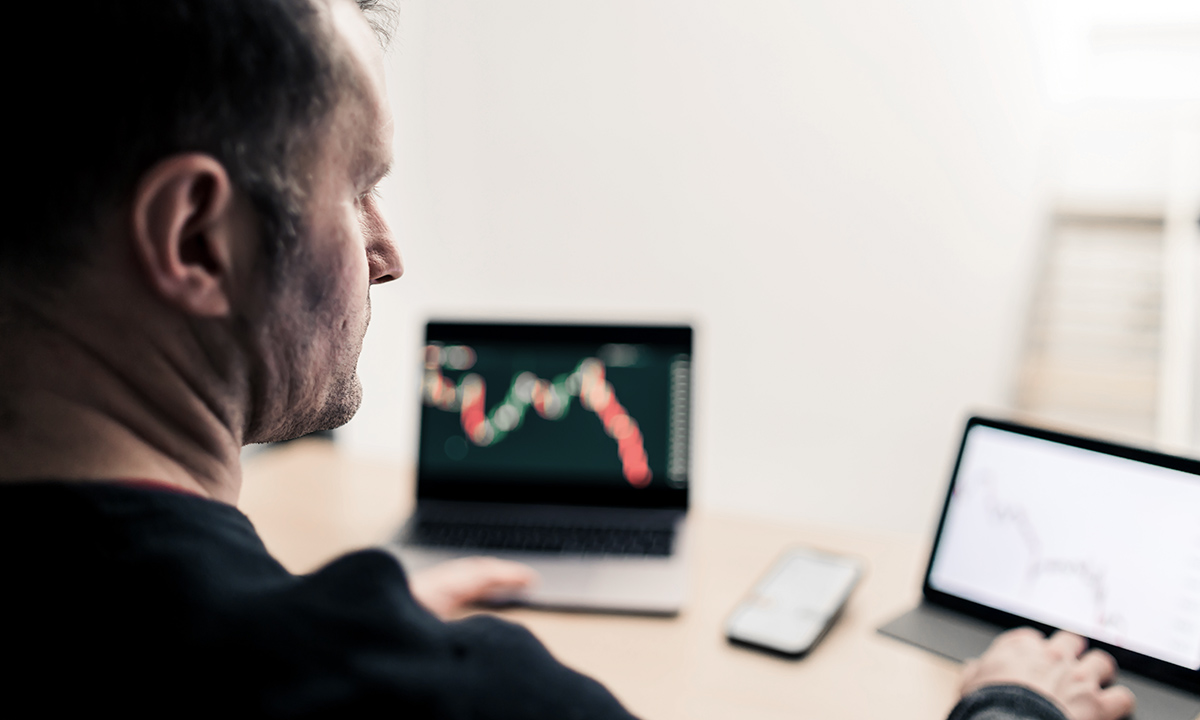 Sad man observing on the various devices the declining value on the candlestick charts